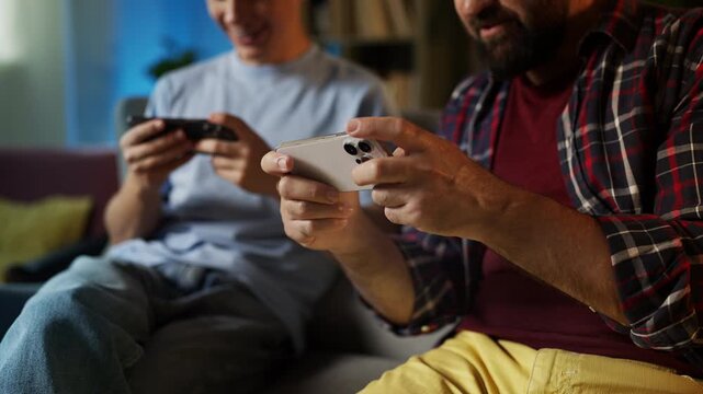 Father and his teenage son playing  online multiplayer game on their phones