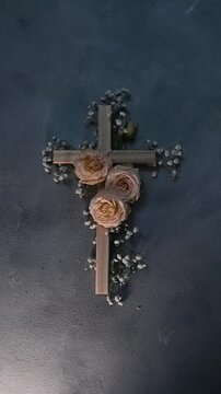 Wooden christian cross vectical with pink roses and gypsophila flowers on a dark wall representing faith and easter resurrection faith, symbolizing