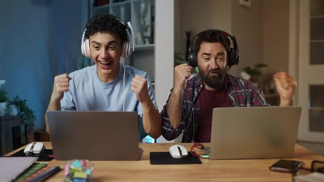 Happy dad and his teen son celebrating a video game victory, bumping fists
