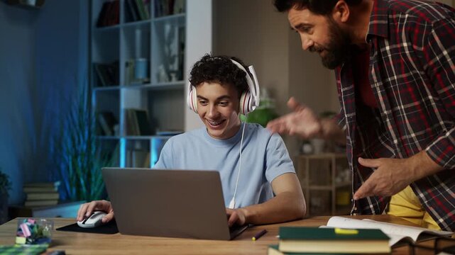 Annoyed father scolding teenage son for playing video games instead of studying