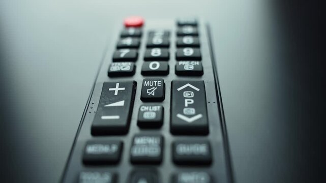 Macro close-up of a TV remote control with navigation keys and colored buttons, shallow depth of field on a dark surface with copy space for streaming and home entertainment concepts.