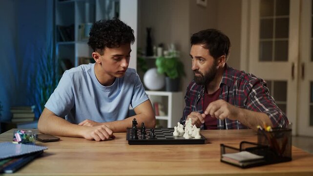Dad teaching his teen son how to play chess, explaining game strategy, pastime