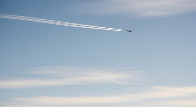 A large commercial passenger jet airplane is captured in silhouette, flying gracefully across a vast, clear blue sky, leaving a pair of long, parallel white contrails trailing distinctly behind it, cr