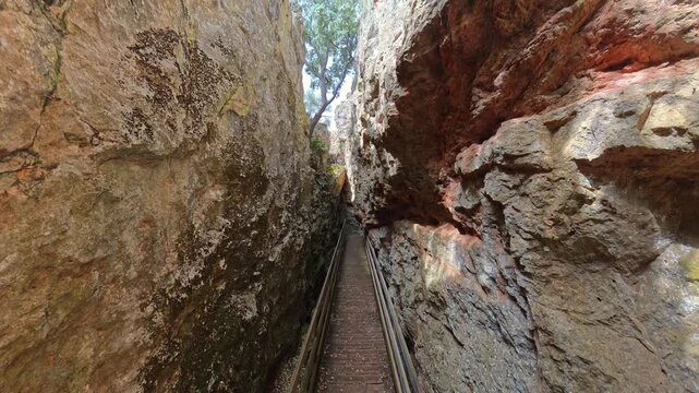 Wooden boardwalk pathway through the narrow walls of the Quebrada del Toro canyon leads forward, offering a unique hiking experience in the natural beauty of Lagunas de Ruidera Natural Park