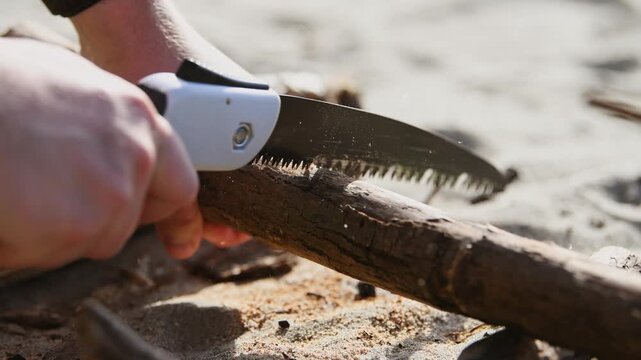 Manual sawing of dry branch on sandy ground with hand saw close-up sequence