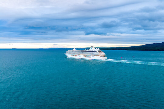 Auckland, New Zealand - 19 February 2026: Aerial view of a luxury cruise ship sailing across the vast, deep blue waters, contrasting with the distant green coastline and the cloudy sky above..