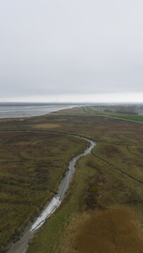Aerial view of a sinuous river snaking through the marshy landscape, where earthy browns meet the muted blues of the distant sea, Nieuw Namen, Zeeland, Netherlands.