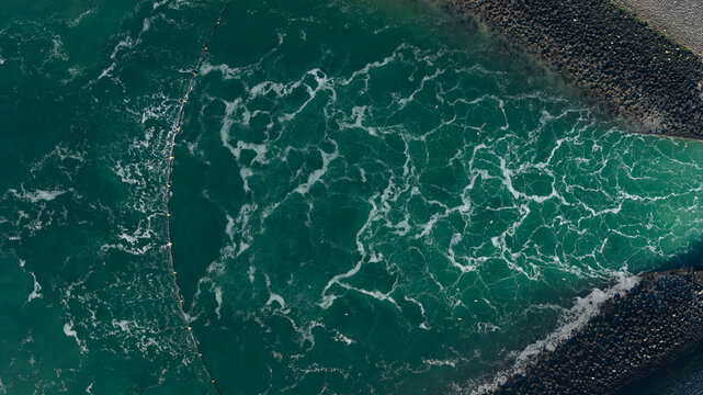 Aerial view of swirling emerald waters caught between stark, rocky banks, a mesmerizing dance of nature's raw power, Ouddorp, Zuid-Holland, Netherlands.