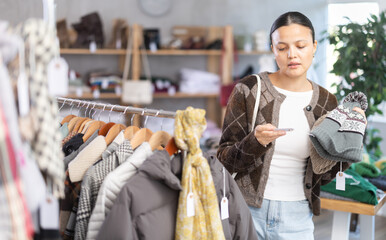 While shopping, Asian woman browsing goods items and choose elect warm hat in store, buyer consider...