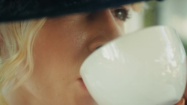 Woman Sipping Coffee. Serene Woman With Blonde Curls Savors Coffee Amidst Soft Cafe Lighting And Warm Ambiance