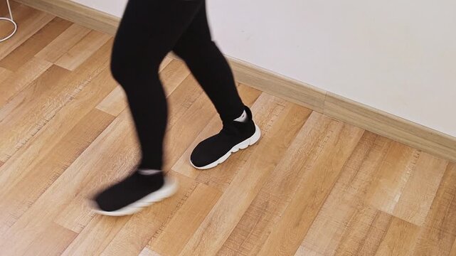 Close-up of person in black leggings and sneakers performing dance steps on wooden floor