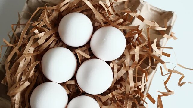 Collection of six white eggs placed in straw on a light surface during daytime