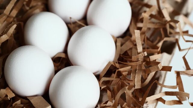 Six white eggs rest on shredded paper in a simple kitchen scene.