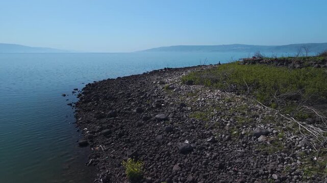 Lake Kinneret in Israel with a drone shot over the rocky Amnon Beach coast and the Golan Heights mountains behind.