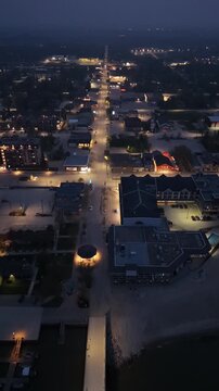 Vertical drone aerial flying forward over Main Street in Gimli Manitoba at night. Small town roadway with streetlights, vehicles and illuminated buildings under dark sky.