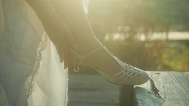 Intimate Moment Of Bride Fixing Her Sandal. Warm Sunrise Illuminates Bride Adjusting Footwear On Dock