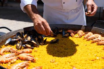 Culinary Artisan at Work: A skilled chef meticulously arranges fresh seafood on a bed of vibrant saffron-infused rice in a large paella pan.