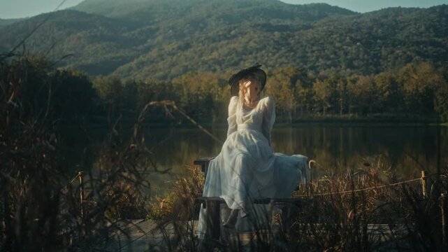 Graceful Woman Dressed In White With Suitcase Taking Slow Walk Near Tranquil Mountain Shoreline