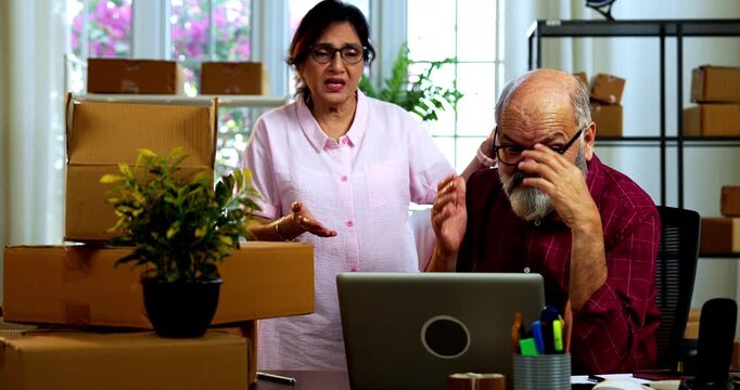 Indian senior couple showing stress doing E-commerce business from home while managing online orders, dispatching parcels, packing cardboard boxes and handling hectic workload in home office