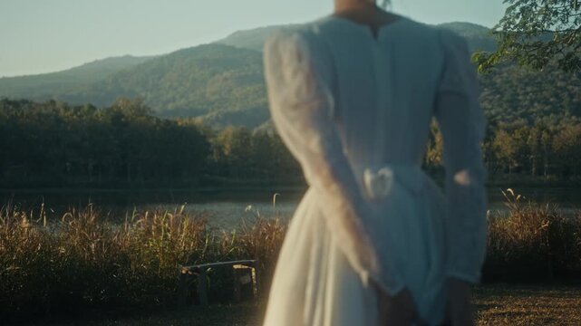 Graceful Woman Dressed In White With Suitcase Taking Slow Walk Near Tranquil Mountain Shoreline