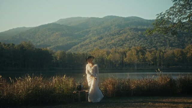 Graceful Woman Dressed In White With Suitcase Taking Slow Walk Near Tranquil Mountain Shoreline