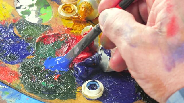 The hands of the artist, work to create creative images in art. Art paints and brushes, applying multi-coloured strokes to the canvas using palette, gouache and watercolour.