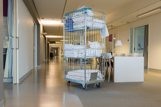 A blanket cart is set up in the hallway of a modern Dutch hospital. It stands next to a waiting area with chairs and tables. Staff may use it for patient comfort.