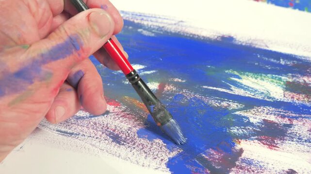 The hands of the artist, work to create creative images in art. Art paints and brushes, applying multi-coloured strokes to the canvas using palette, gouache and watercolour.
