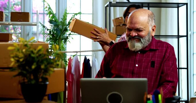Indian senior couple celebrating success in home based E-commerce business while managing online orders, dispatching parcels, packing cardboard boxes and working together in home office