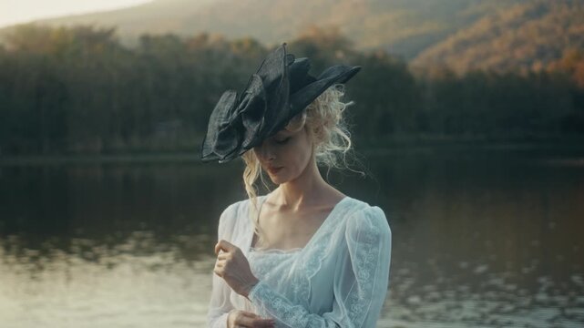 Vintage Lace Dress Adorns Bride Standing By Reflective Water With Mountain Backdrop At Sunrise
