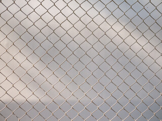 Golden brown chain link fence mesh pattern creating geometric diamond grid texture with soft bokeh...