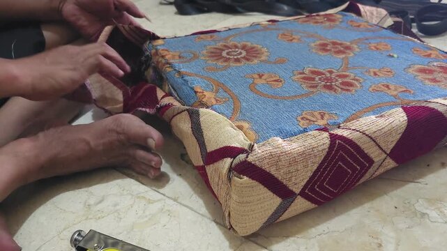 Close-up of an upholsterer using a yellow staple gun to attach floral fabric to a chair seat cushion during furniture restoration