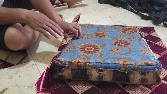 Close-up of a worker using a manual staple gun to upholster a chair cushion with blue floral fabric, demonstrating furniture restoration techniques