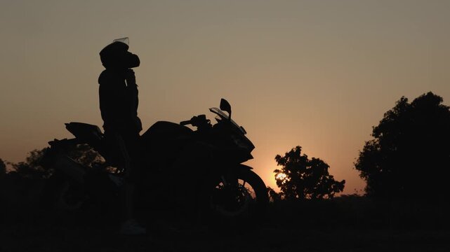 Guy parks motorcycle and takes of helmet at sunset