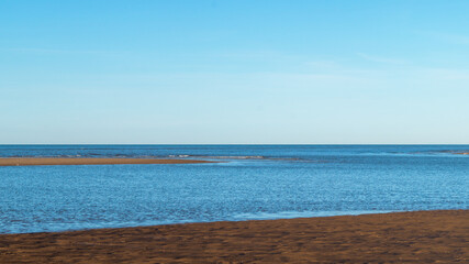Fototapeta premium View of the ocean, sea from the beach with yellow, orange sand. Sea bay. View of the sea horizon on a sunny, clear day