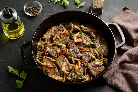 Sauteed liver with butter and onion in pan on black stone background