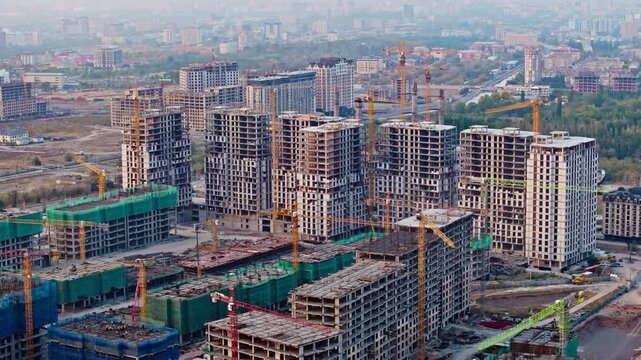 Drone flies backward over construction of multi-storey apartment towers in south Bishkek: unfinished concrete buildings, cranes, green netting amid urban sprawl.