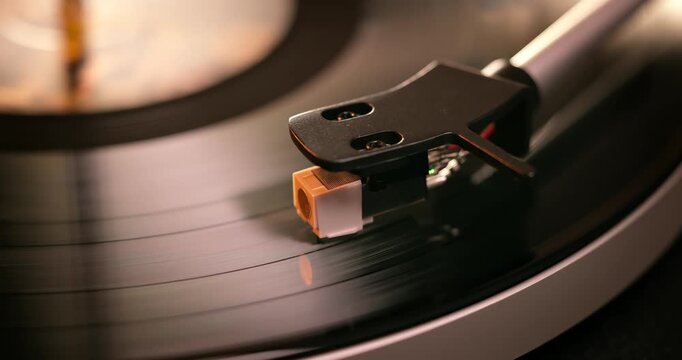 Detailed close-up of a turntable tonearm with white cartridge headshell, positioned over a black vinyl record on the platter, highlighting audio equipment precision.