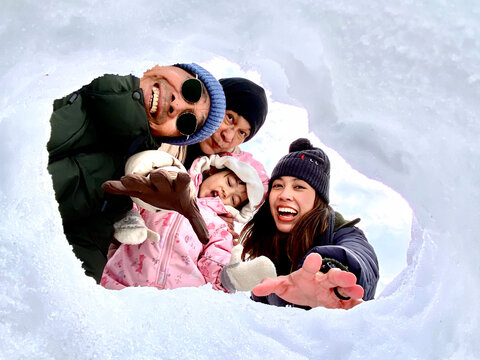 Joyful three-generation Asian family selfie portrait in Japan, featuring grandparents, parents, and a child smiling together through a snow hole, capturing a perfect winter vacation moment.