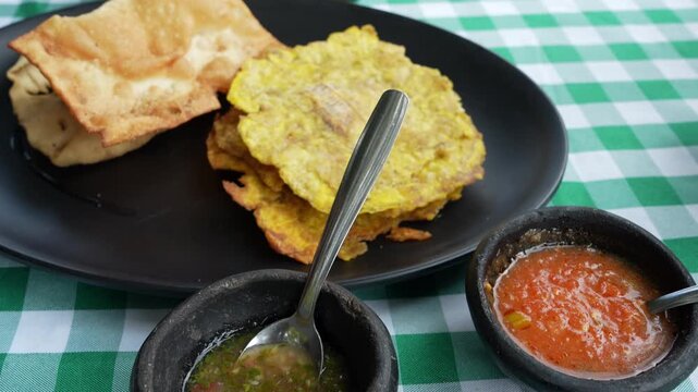 Vibrant close-up of Colombian ojaldras and tostadas artfully presented on a black plate with two traditional sauces, set on a checkered tablecloth. Ideal for cultural and culinary shoots.