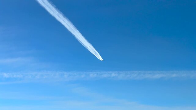 Cockpit view of a jet airplane leaving a white contrail and flying above in a blue sky
