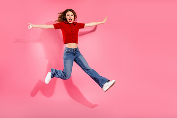 Young chic woman jumps with arms wide on pink background