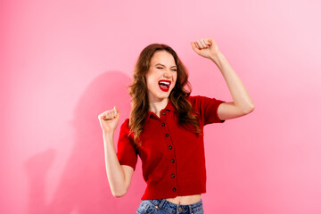 Young chic woman in red polo celebrates with joy against pink background