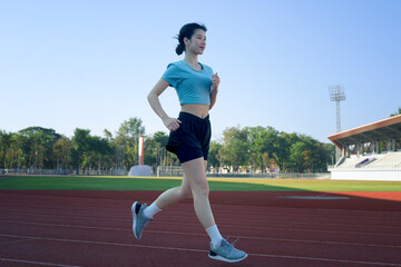 Fototapeta premium Young Asian woman jogging on outdoor running track at stadium, morning exercise