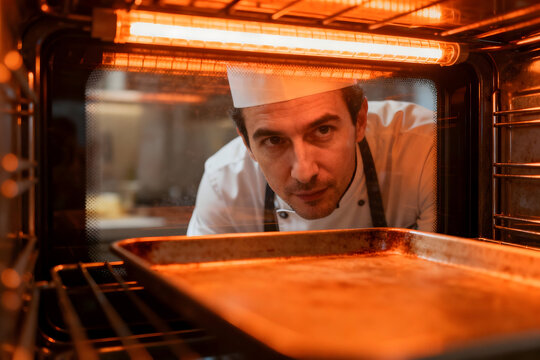 Culinary Observation: A chef intently examines the contents of a preheating oven, embodying the focus and anticipation of a culinary artisan.