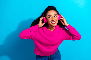 Young woman wearing a pink sweater and headphones smiles against a bright blue background