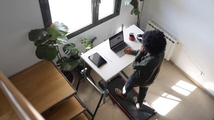 Person multitasking, staying active and focused while working remotely on a laptop at a treadmill desk, blending fitness into a productive home office routine