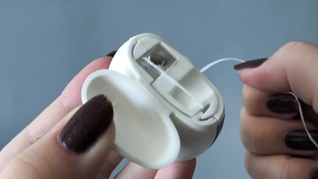 A woman's hands pull out and tear the floss out of the container. Flossing to clean the spaces between your teeth