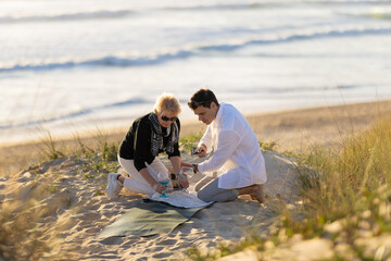 Fototapeta premium Senior woman and young man enjoying beach picnic