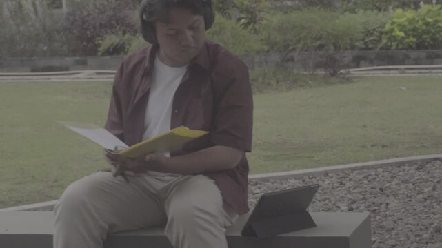 A Southeast Asian student studies at a table in the campus yard with books and a tablet. S-Log3, S-Gamut3.Cine